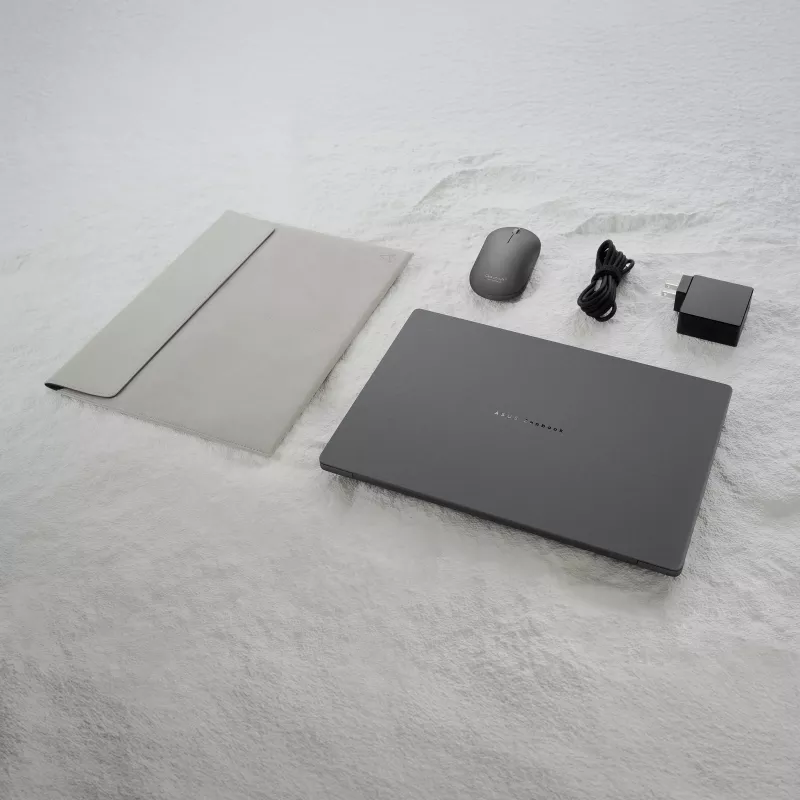 ASUS Zenbook A14 with sleeve, mouse, charger, and cable arranged on surface