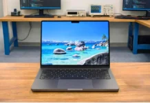 Apple MacBook Pro M5 Review: Full Spes, Real Performance, Battery & Testing Apple MacBook Pro M5 placed on a wooden desk in a professional pcvenus testing lab environment with external monitors in the background