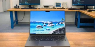 Apple MacBook Pro M5 Review: Full Spes, Real Performance, Battery & Testing Apple MacBook Pro M5 placed on a wooden desk in a professional pcvenus testing lab environment with external monitors in the background