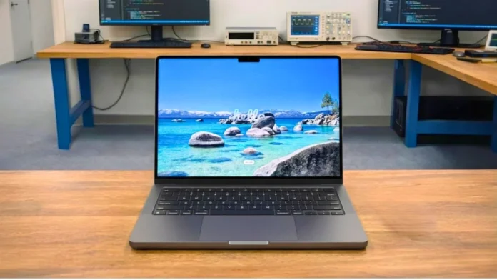 Apple MacBook Pro M5 placed on a wooden desk in a professional pcvenus testing lab environment with external monitors in the background